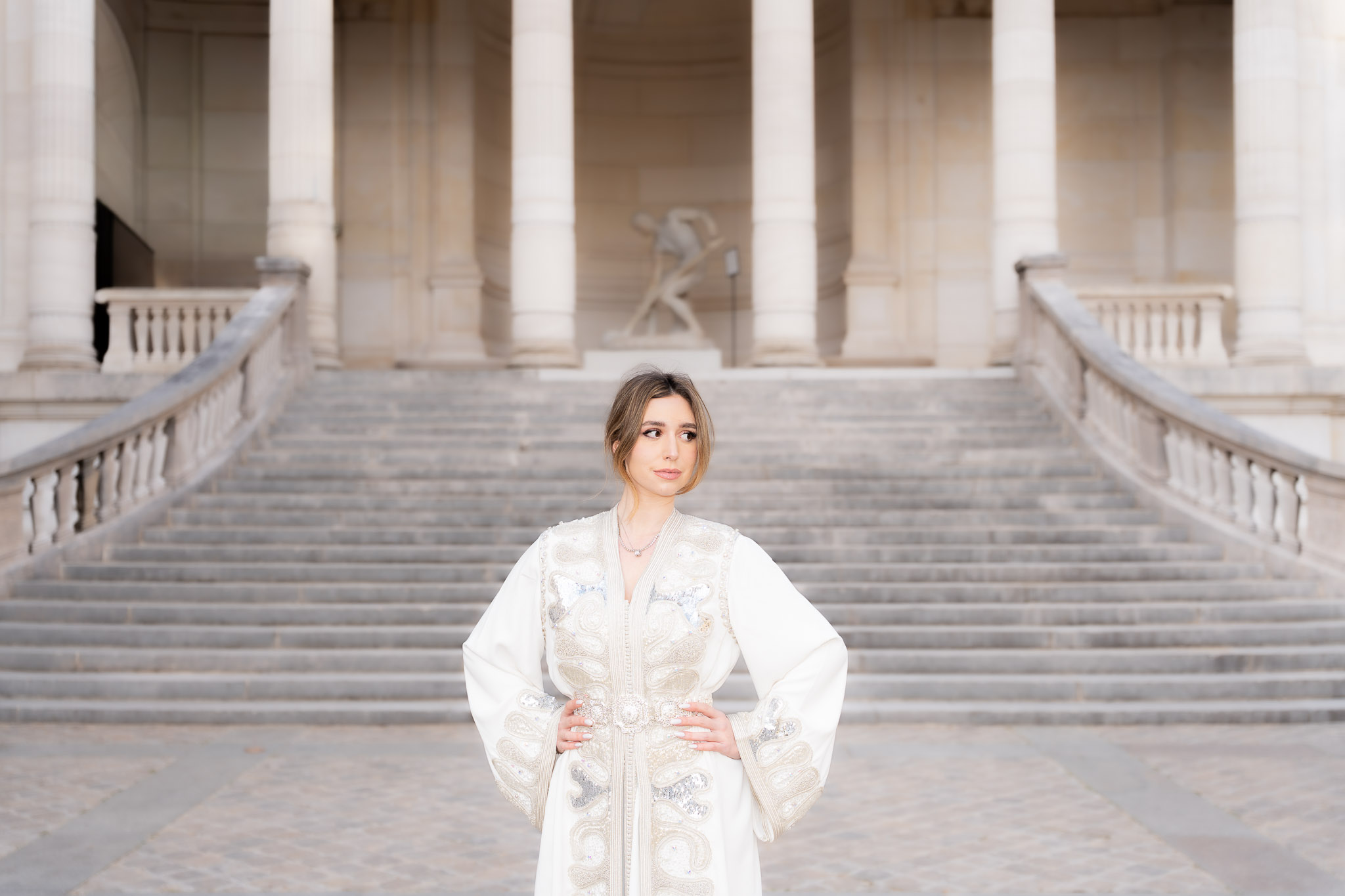 Woman in a traditional embroidered caftan posing on a staircase during an editorial shoot in Paris