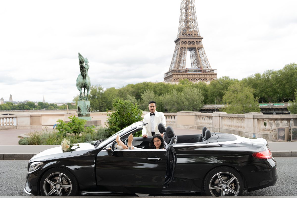Bride and groom in a convertible car near the Eiffel Tower after their wedding in Paris