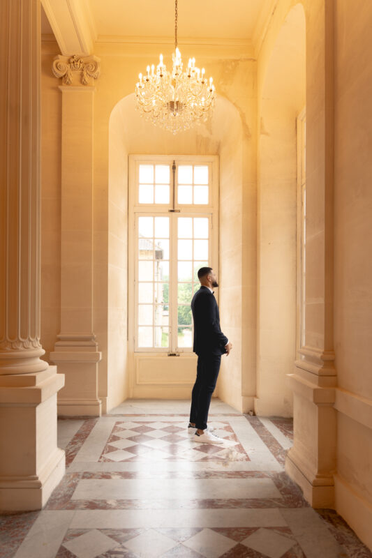 Groom standing by tall windows during a luxury wedding at Château de Saint-Martin-du-Tertre
