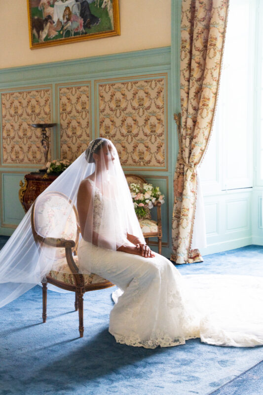 Bride seated in a château room wearing her veil during her wedding day