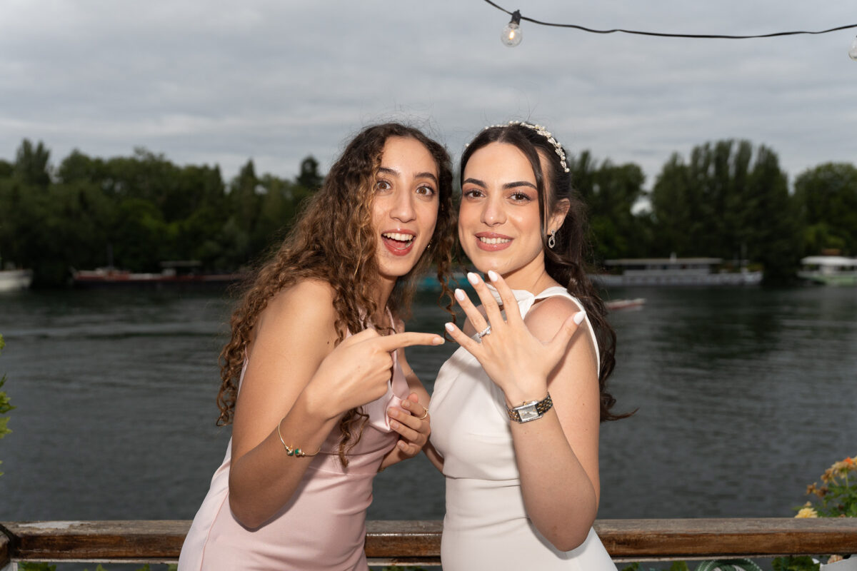 Bride and bridesmaid showing their rings by the river after a wedding in Île-de-France