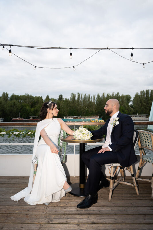Bride and groom seated by the river after their wedding in Île-de-France