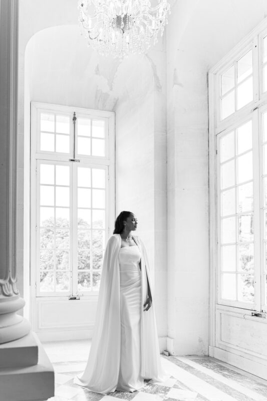 Black-and-white portrait of the bride by tall windows during a château wedding