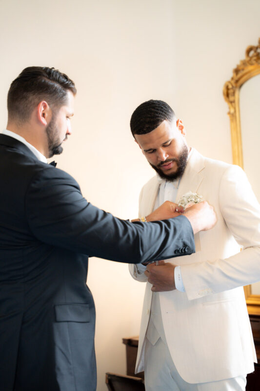 Groomsman helping the groom adjust his suit during wedding preparations